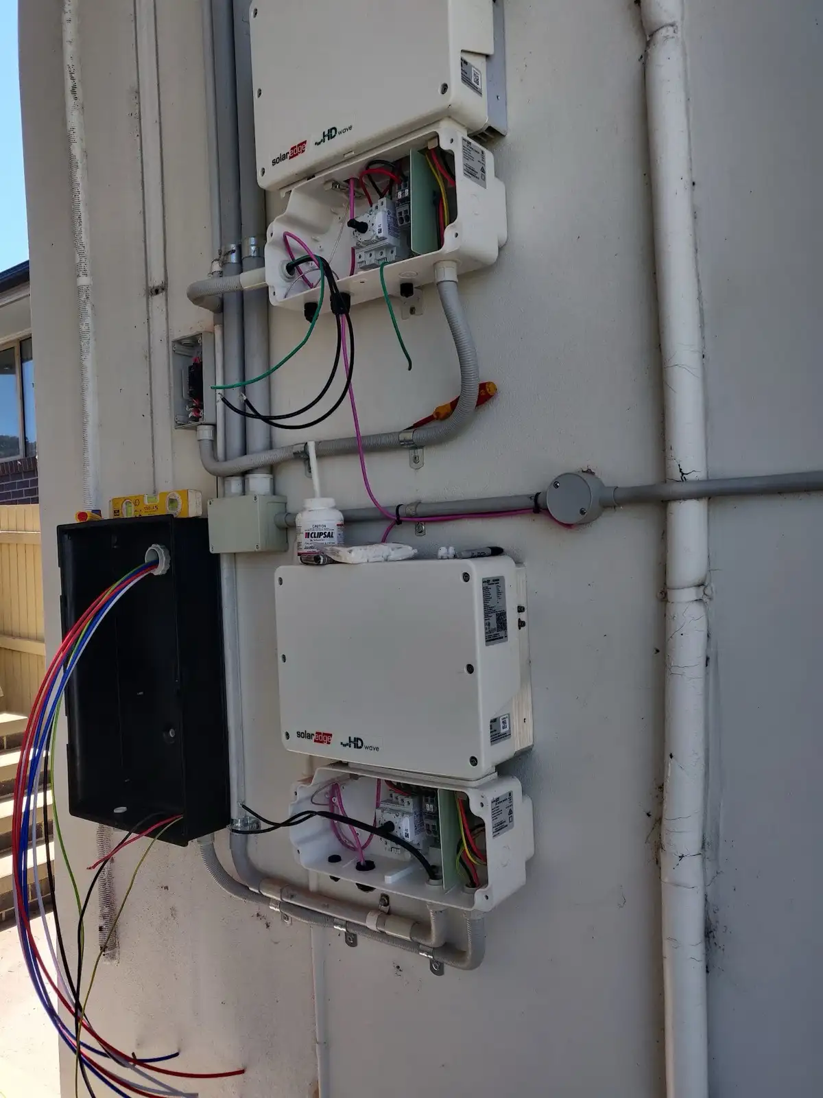 Two SolarEdge inverters and their isolators being wired on an outside wall, conduit already run and clipped.