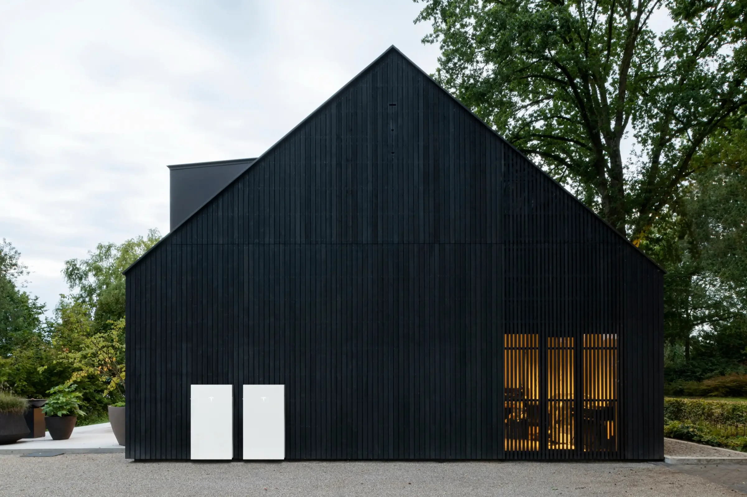 Two Tesla home batteries mounted against the wall of a dark timber barn.