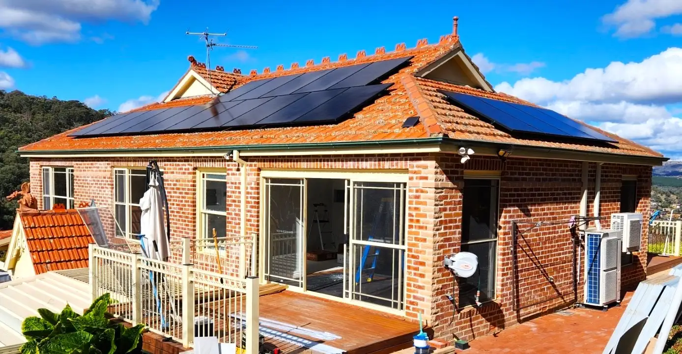 Black panels across the tiled roof of a red brick house, hills behind and a deck in the foreground.