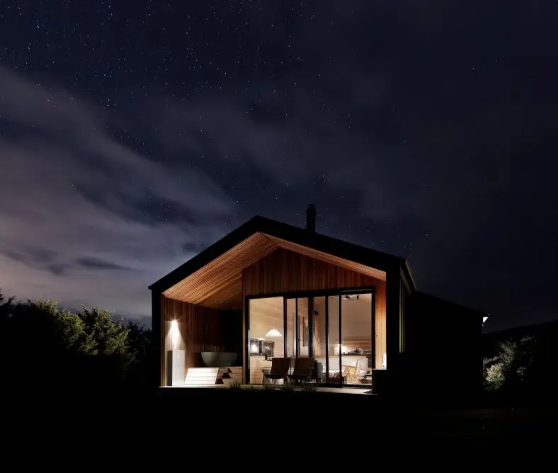 A single-storey house at night with its interior lights on behind full-height glazing, under a clear sky