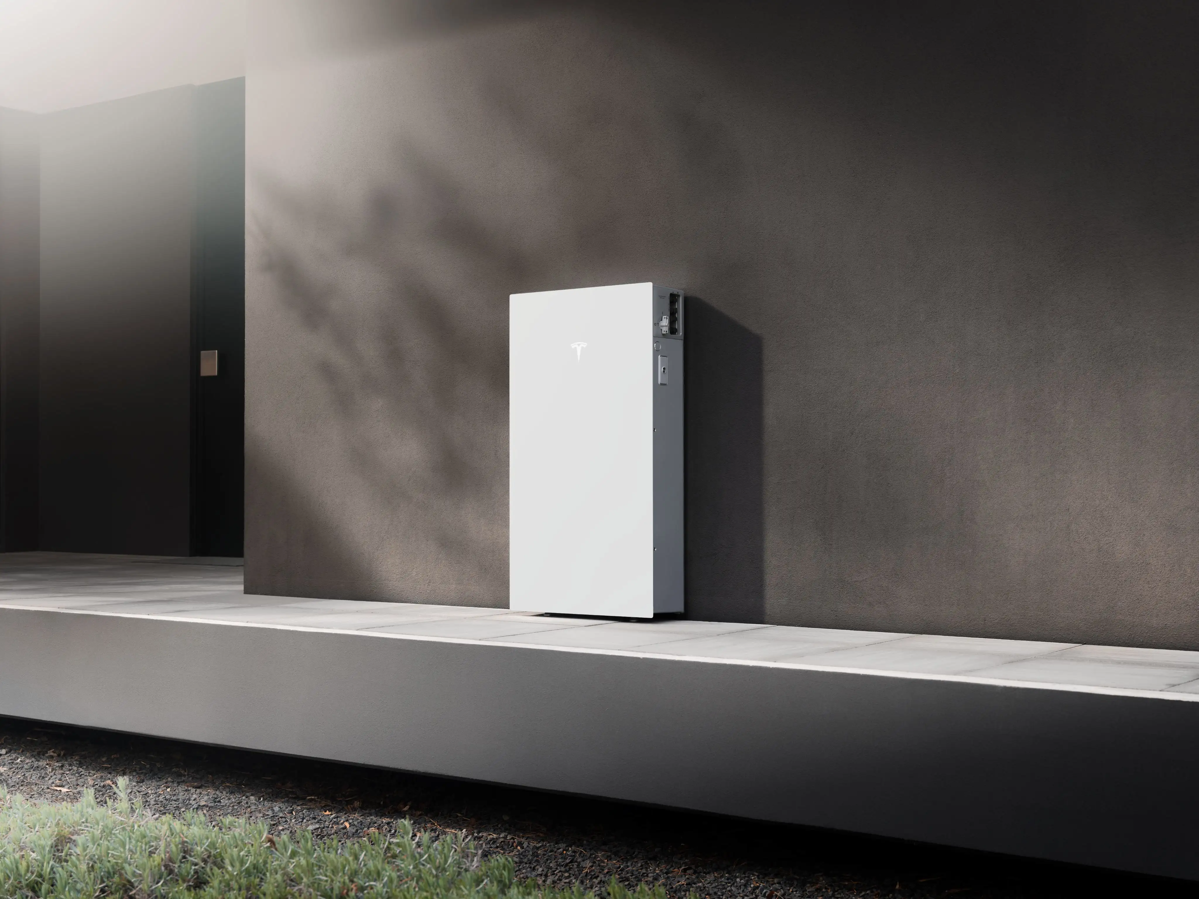 A white Tesla Powerwall 3P standing on a concrete plinth against a dark wall, in raking light